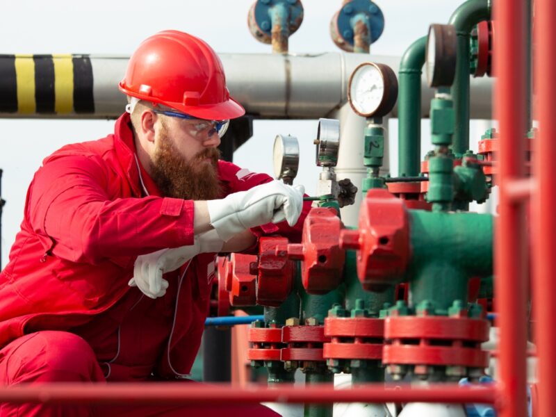 Commercial Gas Certificates | Commercial Gas Pipework Engineer in red overalls, hard hat and safety glasses inspecting pressure gauges and valves on gas pipework